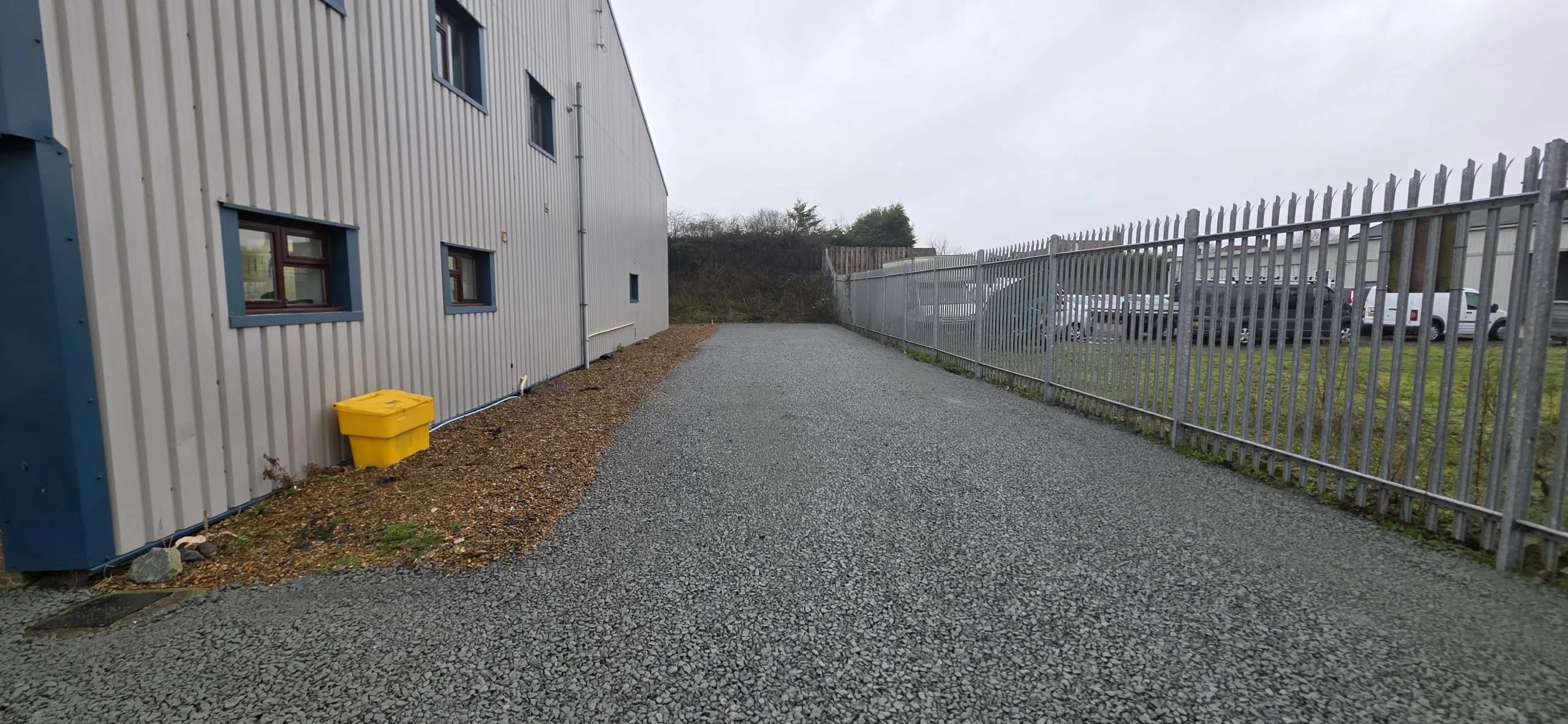 Completed compacted aggregate access road beside an industrial building