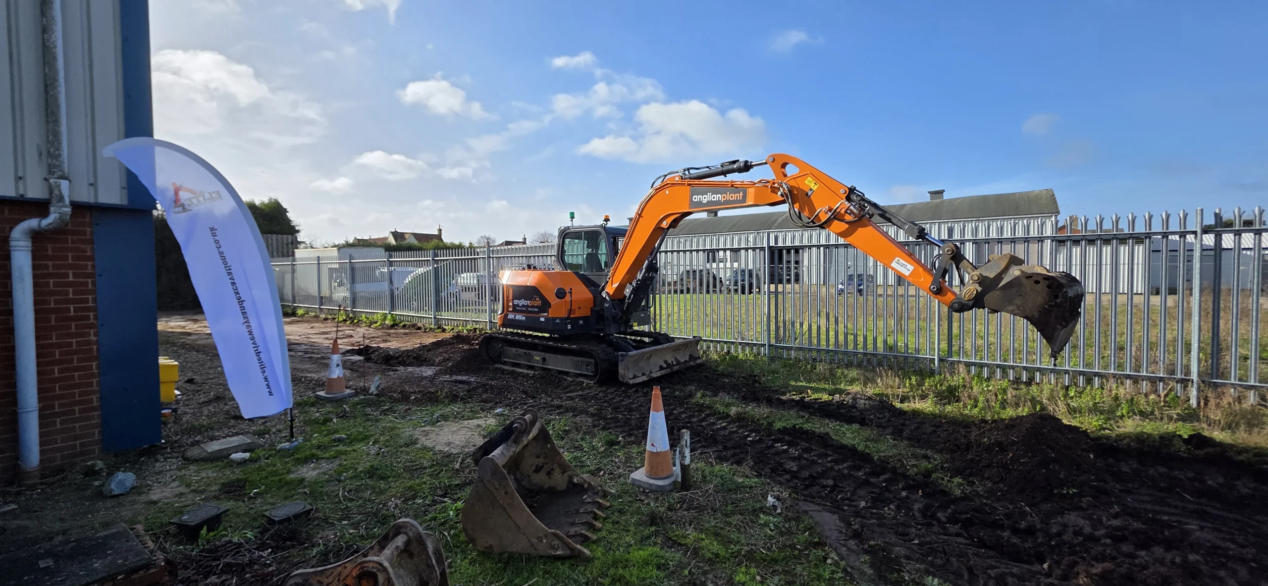 Tracked excavator carrying out commercial groundworks beside a secure industrial site